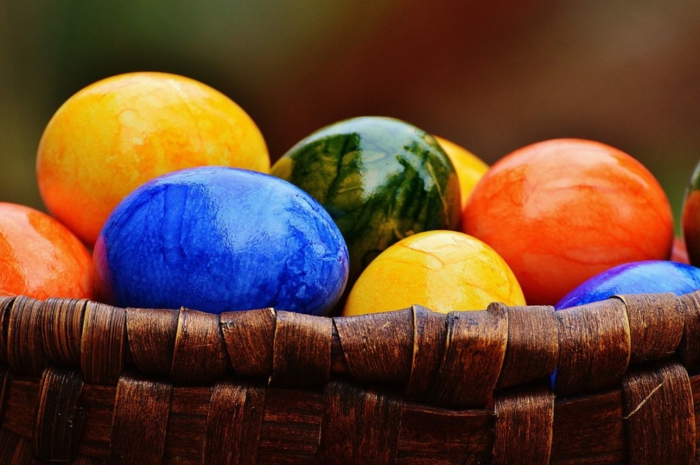 ein Körbchen voller bunte Eier, blau in Vordergrund, zwei gelbe und orange und grünes in Hintergrund