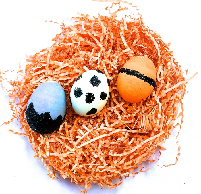 drei gefärbte Ostereier, blaue, orange, und weiße Eier mit glätzender schwarzer Farbe dekoriert